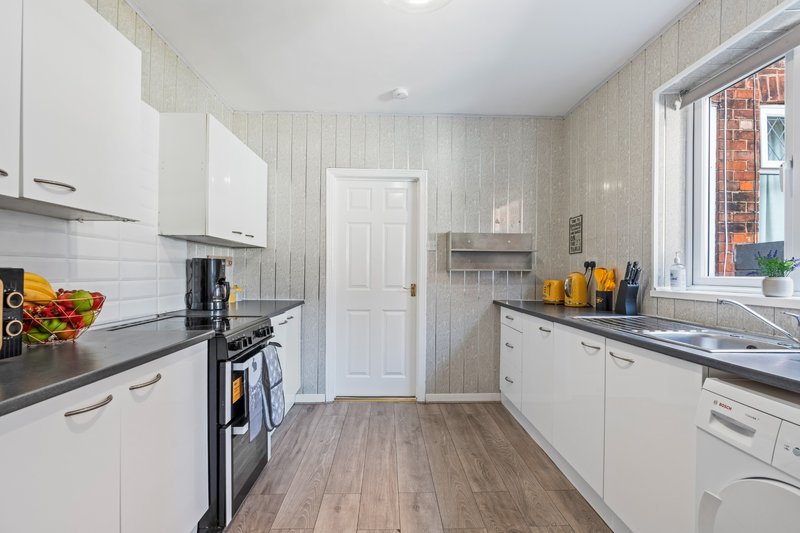 Modern kitchen with white cabinetry, black countertop, stove, and window overlooking brick building