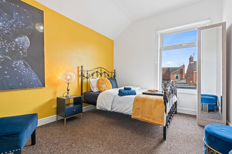 Bright yellow bedroom with single metal bed, blue accents, and city views from balcony door