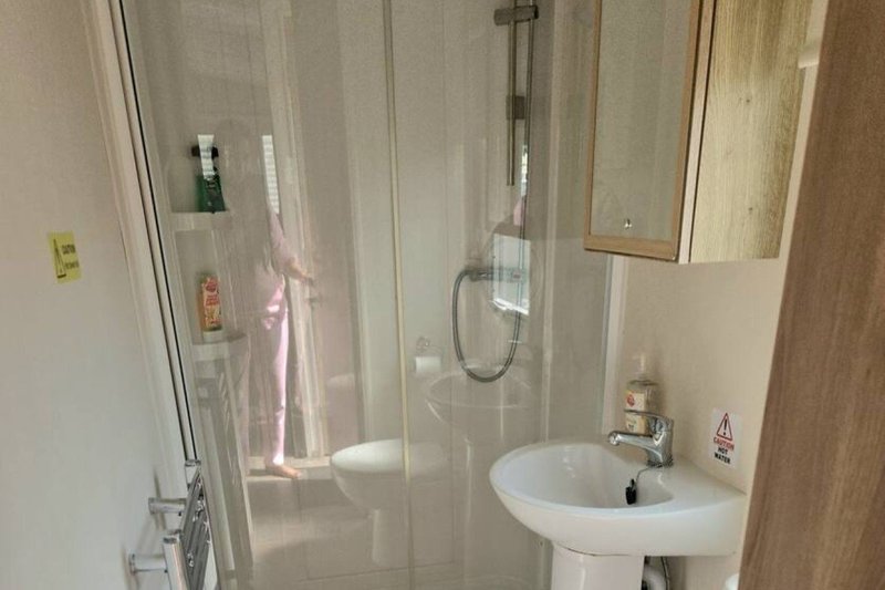 Modern bathroom with pedestal sink, glass shower enclosure and wooden vanity mirror