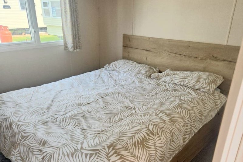Bedroom with double bed, patterned bedding, wooden headboard and window with curtains