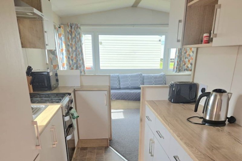Modern galley kitchen with white cabinetry, stainless steel kettle, and view into bedroom area