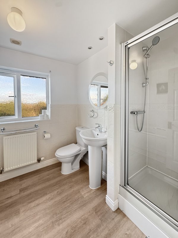 Modern bathroom with white suite, shower enclosure, pedestal sink and wooden floor