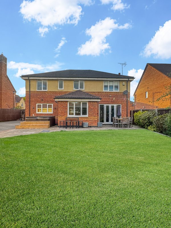 Modern brick detached house with manicured lawn, patio area, and clear blue sky