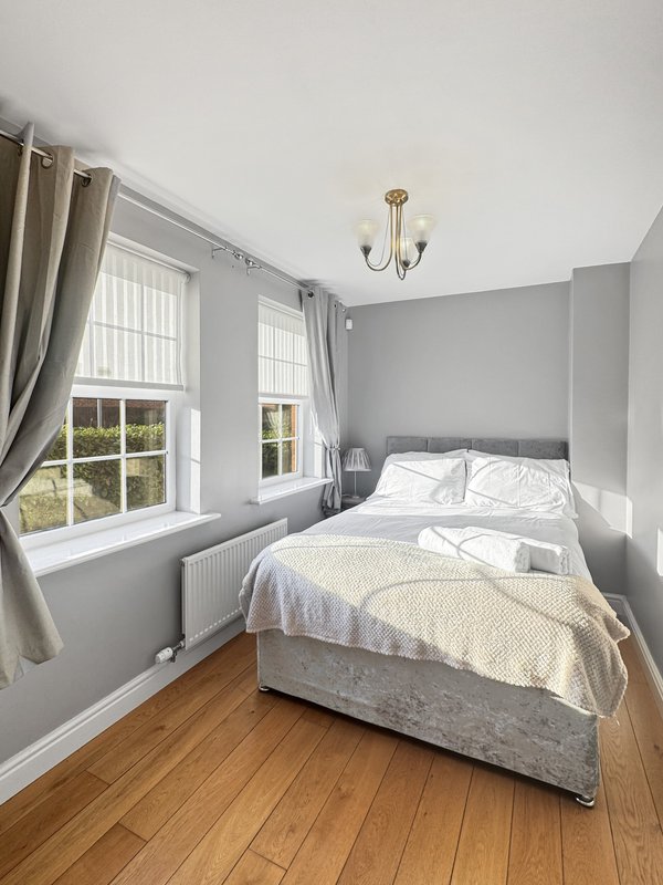 Bright bedroom with double bed, gray walls, wooden floor and large windows