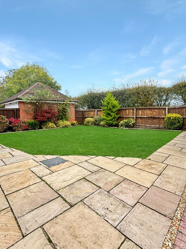 Rear garden with paved patio, manicured lawn, wooden fence and mature trees