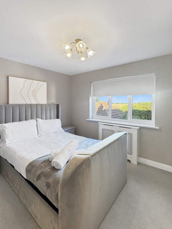 Modern bedroom with upholstered bed, ceiling light, and large window with countryside view