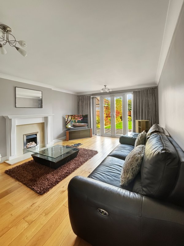 Bright living room with black leather sofa, fireplace, glass coffee table, and garden doors with autumn views
