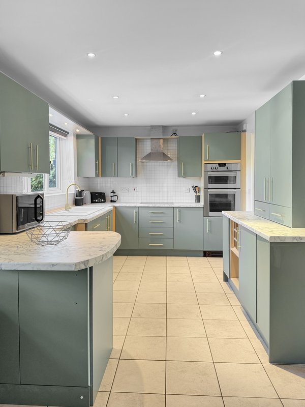 Modern kitchen with sage green cabinetry, marble countertops, island, and stainless steel appliances