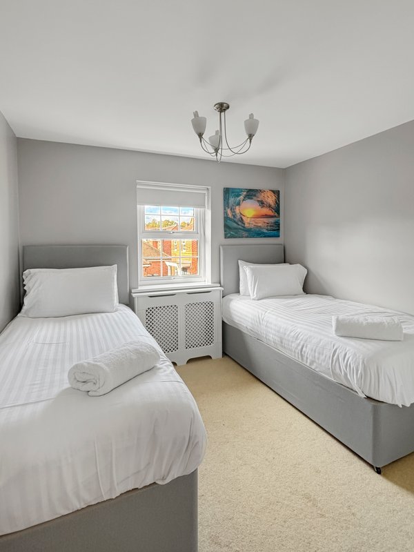 Twin bedroom with two single beds, window, ceiling light fixture and wall art
