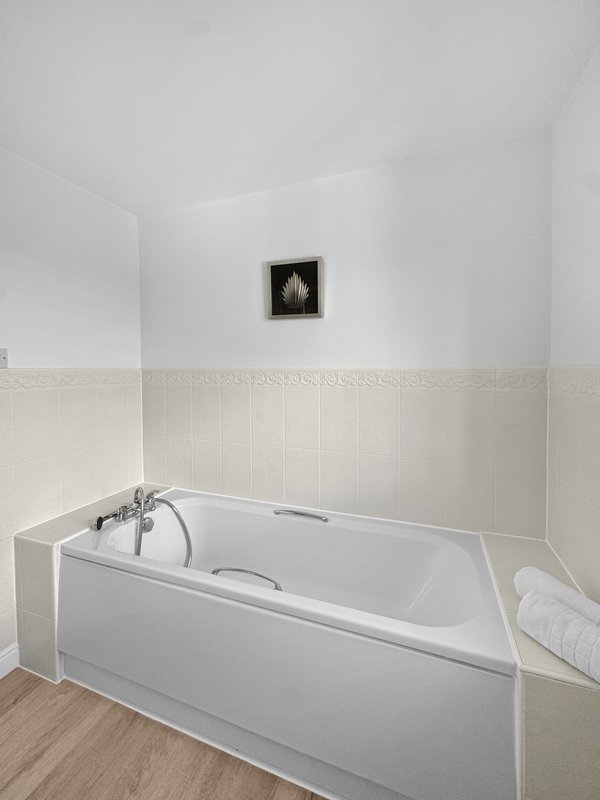 Modern bathroom with white bathtub, cream wall panelling, and small framed artwork