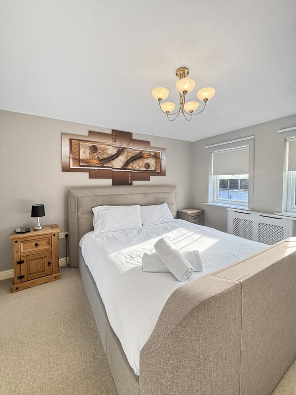 Bright bedroom with double bed, wooden nightstand, ceiling light fixture and window