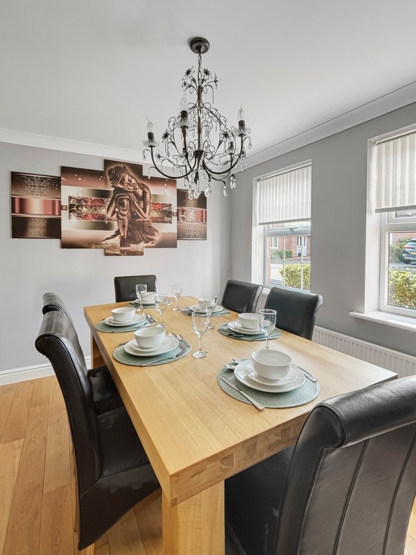 Dining room with wooden table, black chairs, chandelier, and wall art