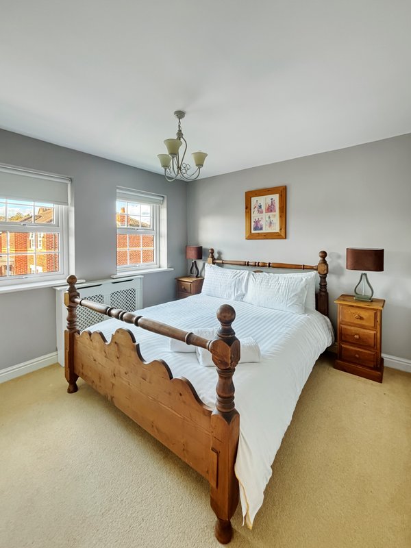 Bright bedroom with wooden four-poster bed, white bedding, wooden nightstands, and large windows