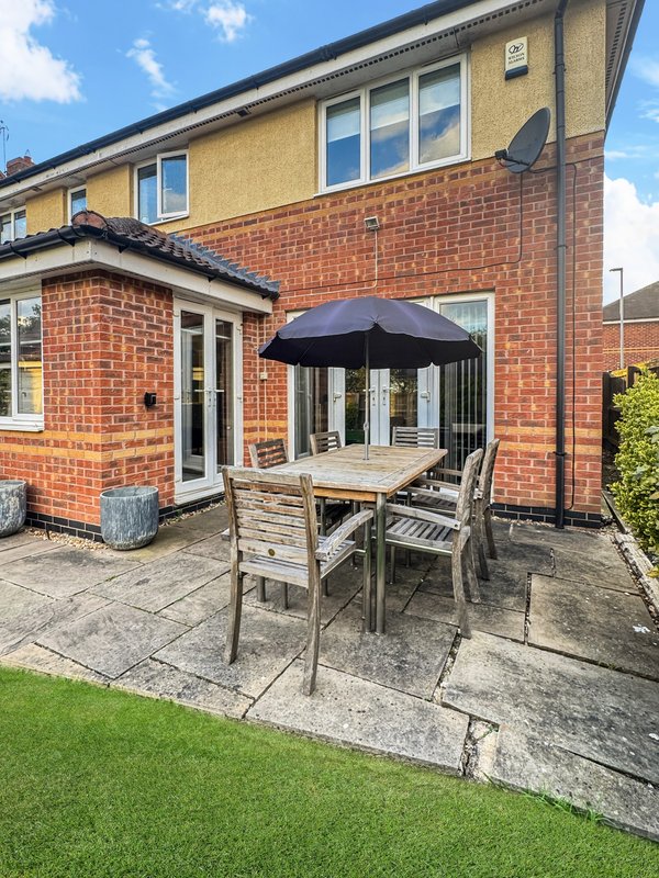 Brick house with patio area, dining table, umbrella, and manicured garden