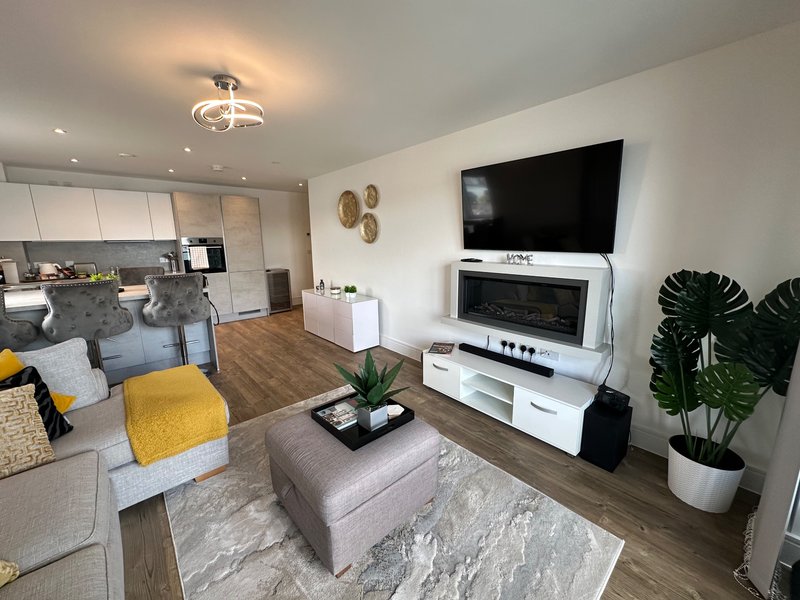 Modern living room with grey sofa, yellow accents, TV, fireplace and open-plan kitchen