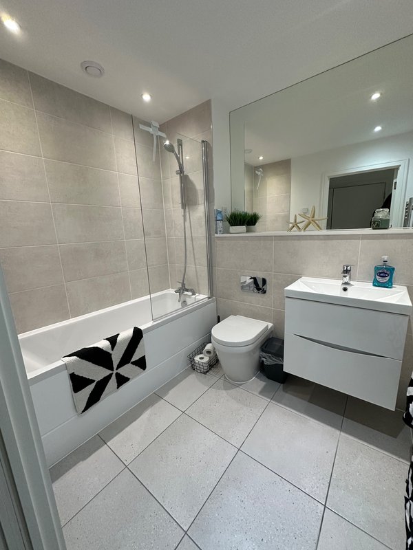 Modern bathroom with shower bath, white vanity, toilet, large mirror and tiled flooring