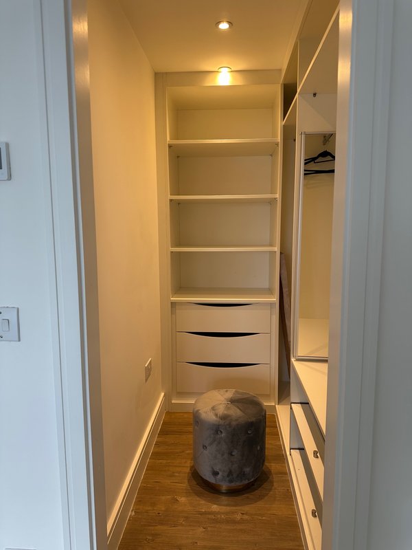 Walk-in closet with built-in shelving, drawers, and storage ottoman on wooden floor