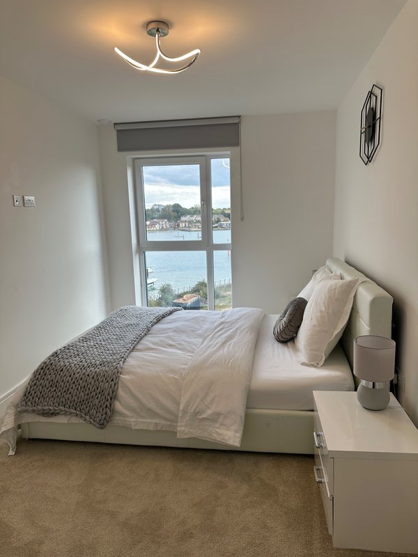 Bright bedroom with single bed, large window overlooking water, ceiling light fixture