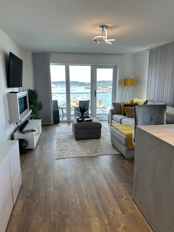 Modern open-plan living room with water view, gray sofa, TV, and yellow accent cushions
