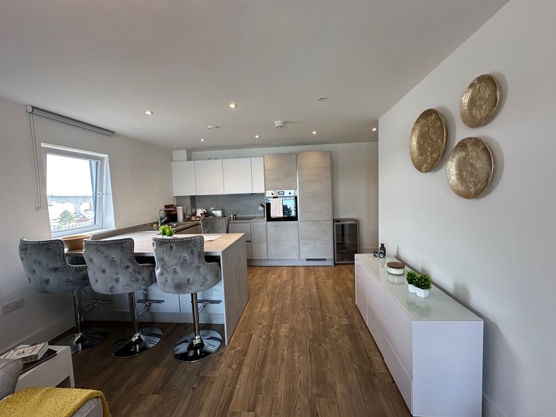 Modern kitchen and dining area with grey cabinetry, wooden flooring, bar seating, and wall decor