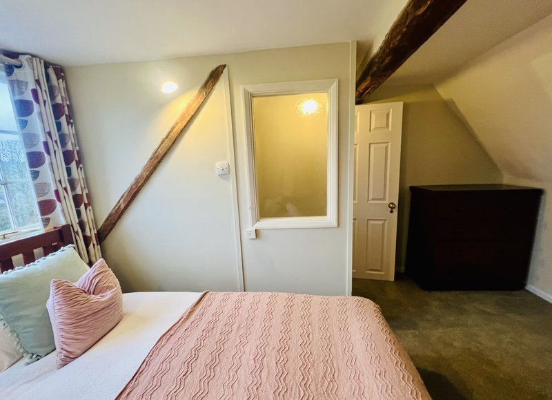Attic bedroom with double bed, pink bedding, exposed beams, and TV in corner