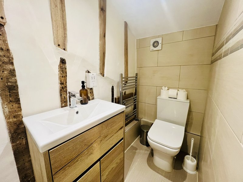 Modern bathroom with wooden vanity, white sink, toilet, heated towel rail and beige tiling
