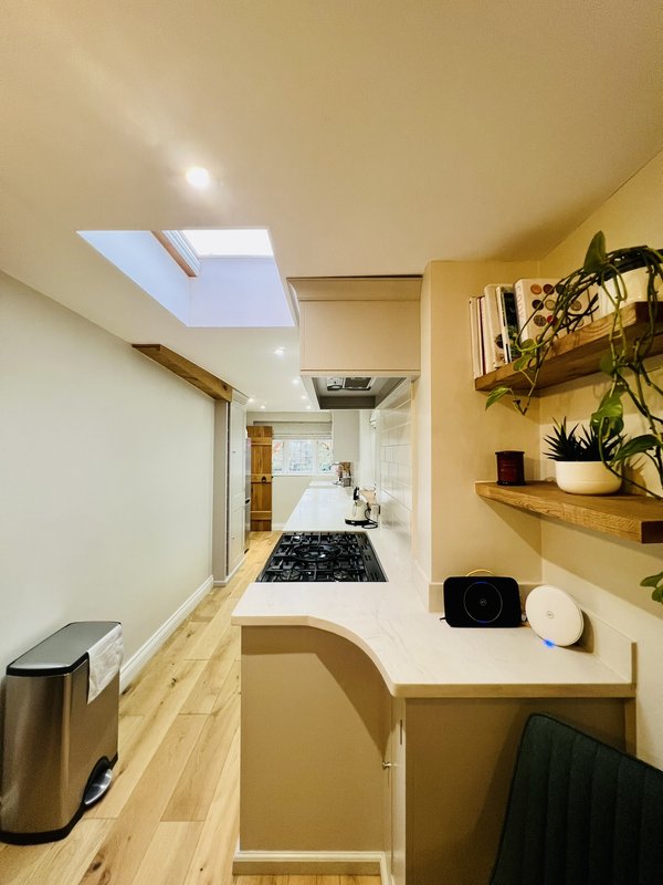 Narrow kitchen with skylight, wooden countertops, stainless steel bin and potted plants on shelves
