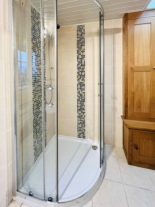 Modern bathroom with curved glass shower enclosure, black and white tile accent, and wooden cabinetry