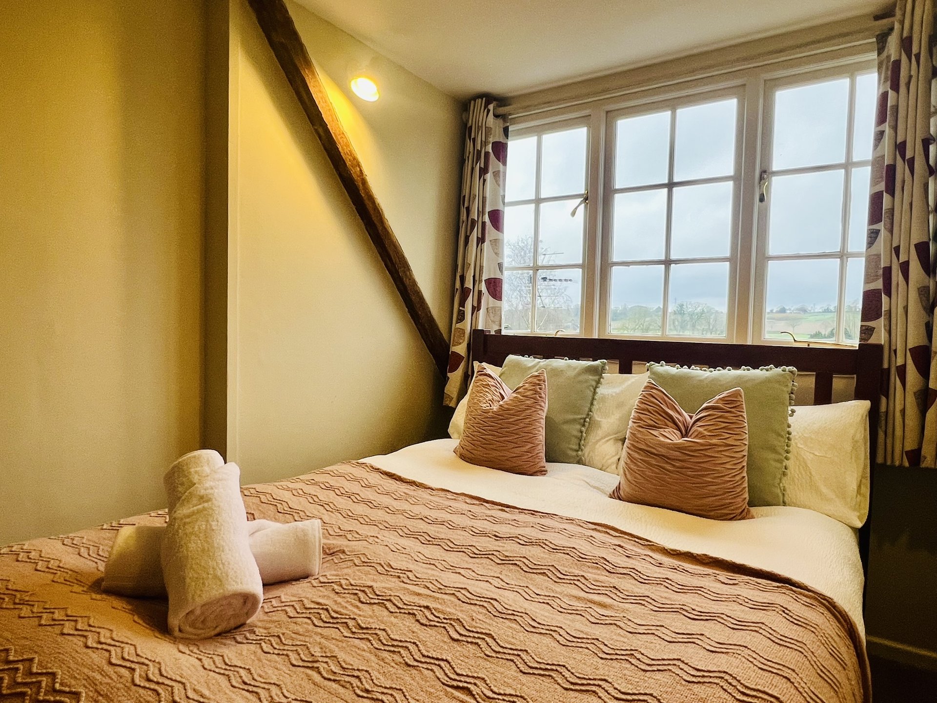 Bright bedroom with double bed, decorative pillows, large window with countryside views