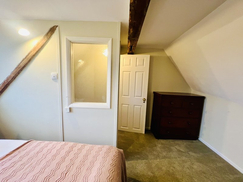 Attic bedroom with single bed, exposed beam, bathroom door and television.