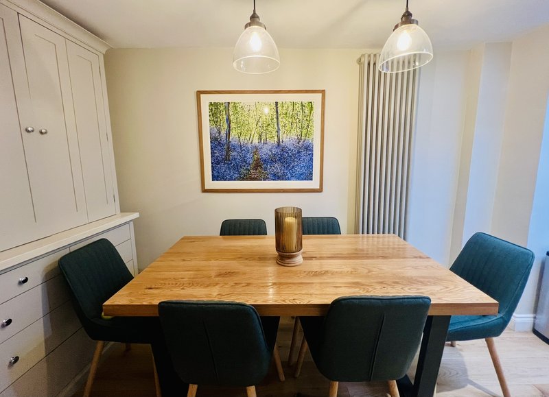 Dining room with wooden table, black chairs, framed landscape artwork, and pendant lights