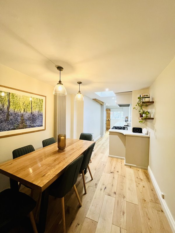 Open-plan dining and kitchen area with wooden table, black chairs, pendant lights, and light wood flooring