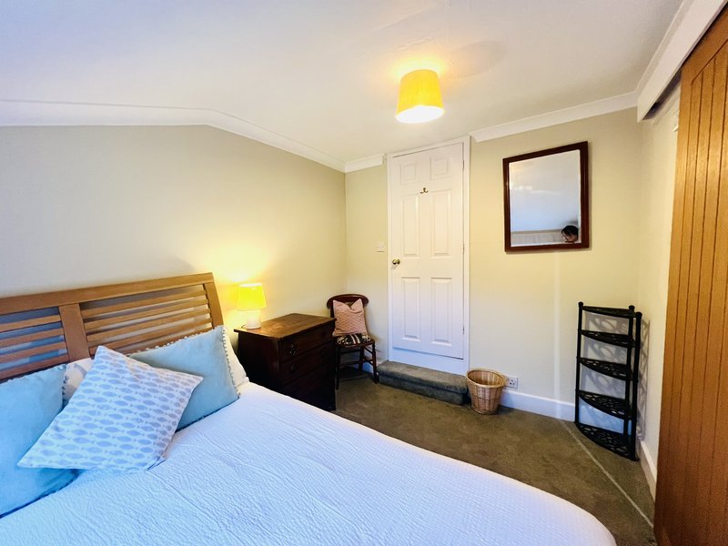 Bedroom with wooden bed frame, blue bedding, yellow lamps, white door and framed window art.
