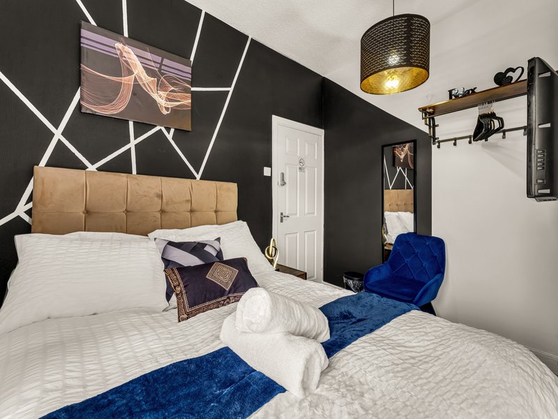 Modern bedroom with two beds, tan headboard, dark accent wall, pendant light and shelving