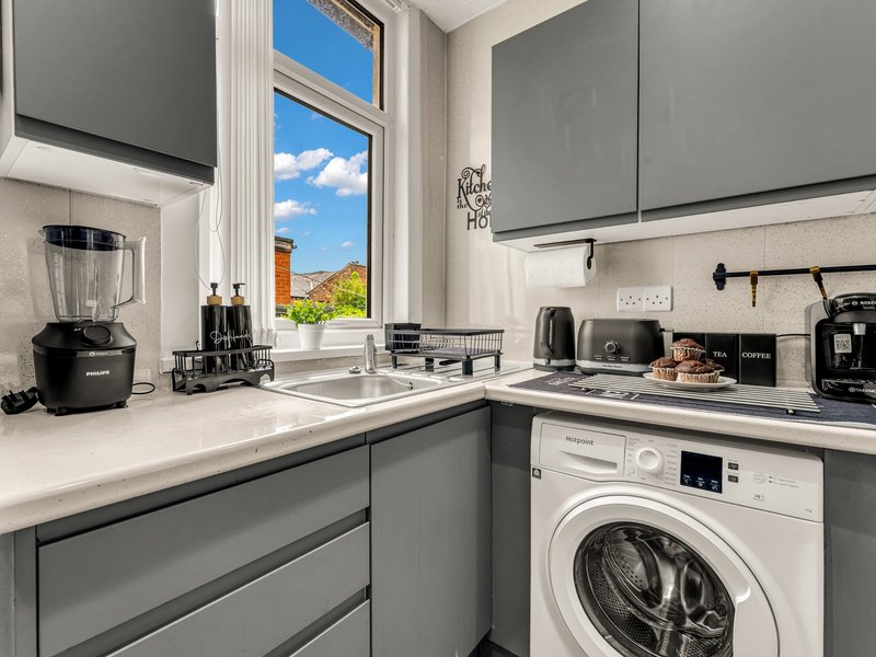 Modern kitchen with gray cabinetry, white countertops, washing machine, and large window with garden view