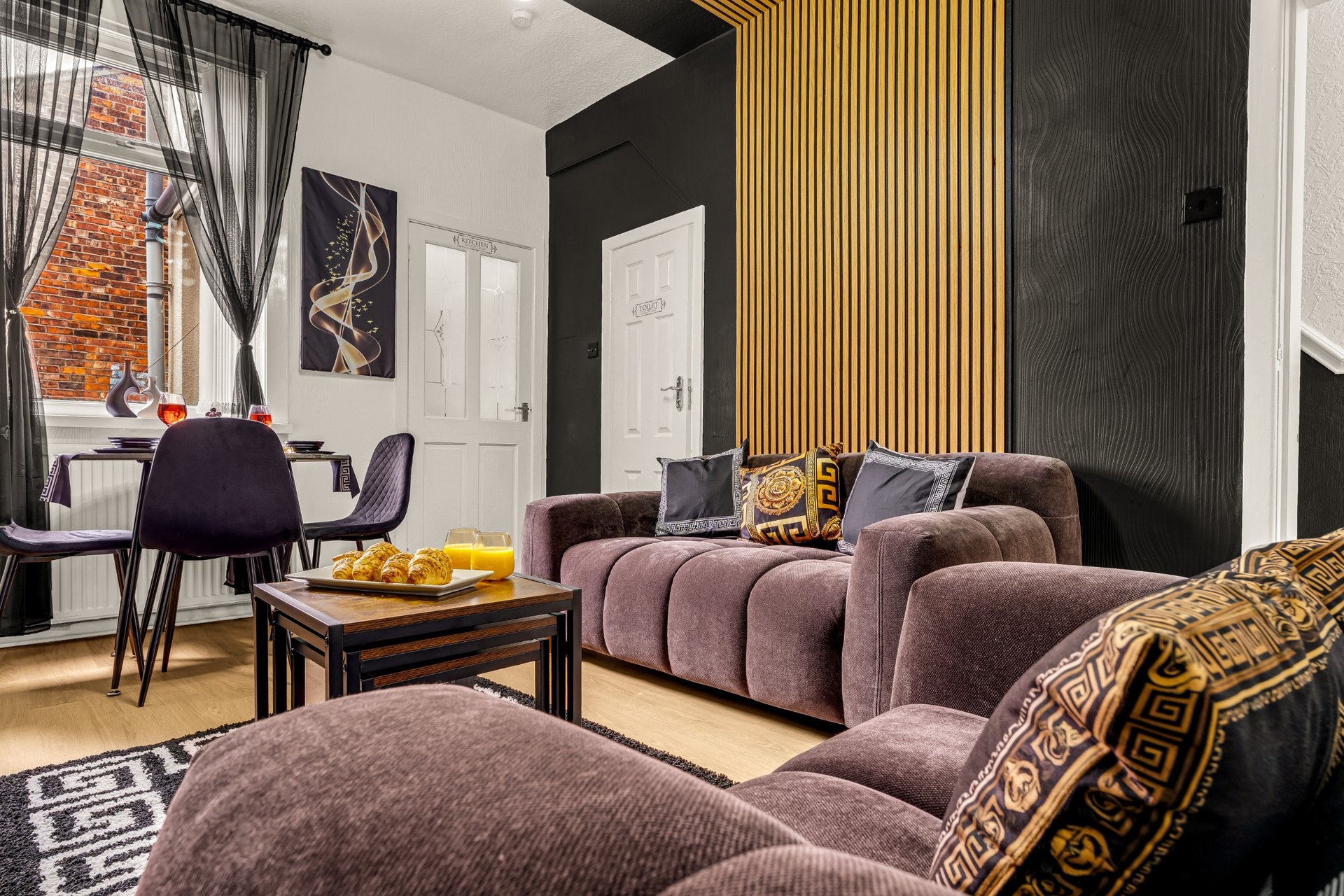 Modern living room with purple upholstered sofa, dining table, black accent wall and gold paneling