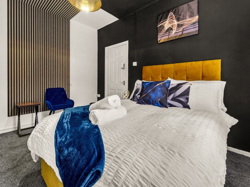 Modern bedroom with double bed, yellow headboard, blue velvet throw, and dark accent wall