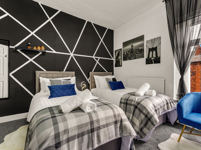 Modern twin bedroom with geometric black accent wall, plaid bedding, and blue armchair