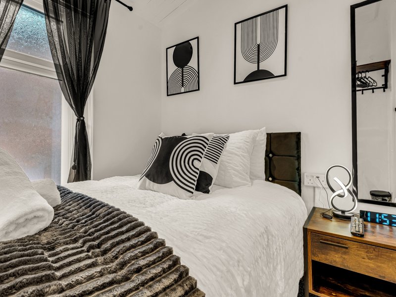 Modern bedroom with white bedding, black and white geometric cushions, wooden bedside table and wall art