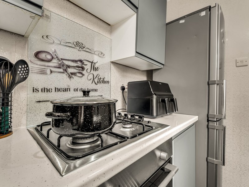 Modern kitchen with gas cooktop, pot, black air fryer, stainless steel fridge and decorative wall text