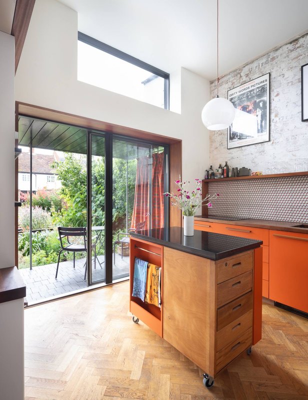 Modern kitchen with orange cabinetry, wooden island, and garden view through glass doors