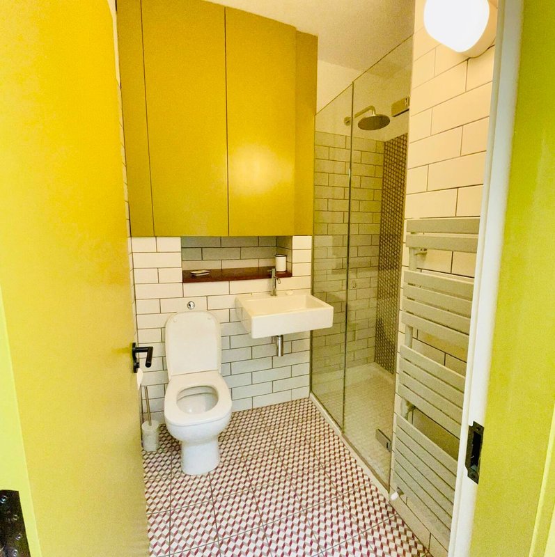 Modern bathroom with yellow walls, white subway tile, geometric floor, toilet, sink and shower enclosure