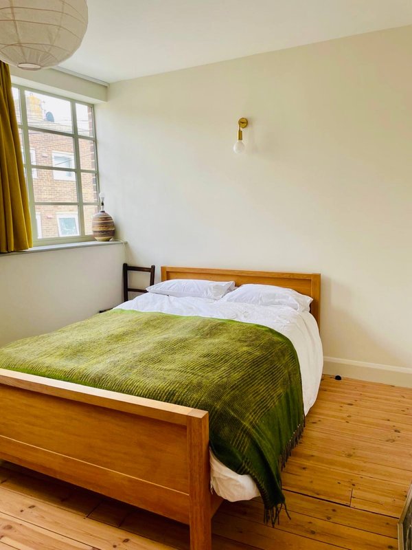 Bedroom with wooden bed, green bedcover, white pillows and wooden floor