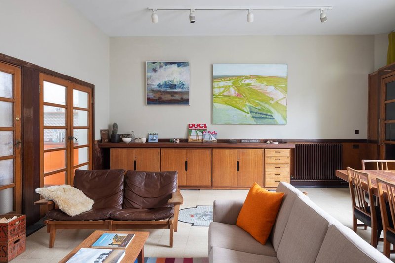 Open-plan living room with brown leather sofa, gray armchair, wooden sideboard and dining table