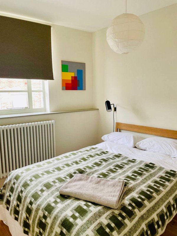 Bright bedroom with double bed, green striped bedding, colorful wall art, and pendant light