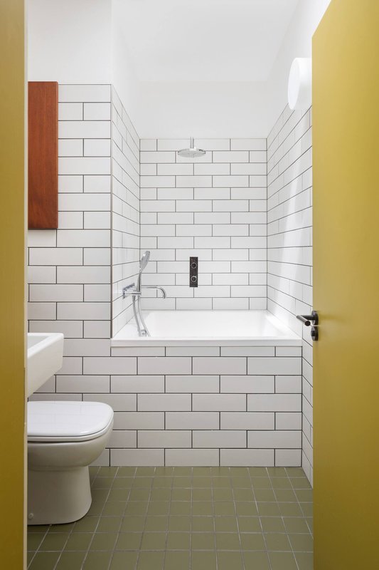 Modern bathroom with white subway tile walls, bathtub, toilet, and yellow door frame