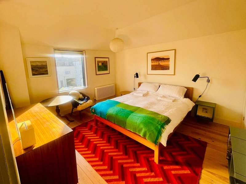 Bright bedroom with double bed, colorful bedding, wooden floor, red rug and wall art