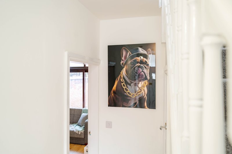 Bright hallway with white walls, framed dog portrait artwork, and open doorway to bedroom