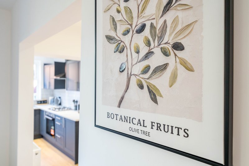 Hallway with framed botanical print and view into modern kitchen with dark cabinetry