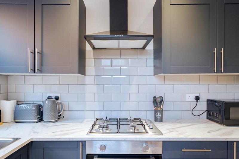 Modern kitchen with dark cabinetry, white subway tile backsplash, gas cooktop and range hood